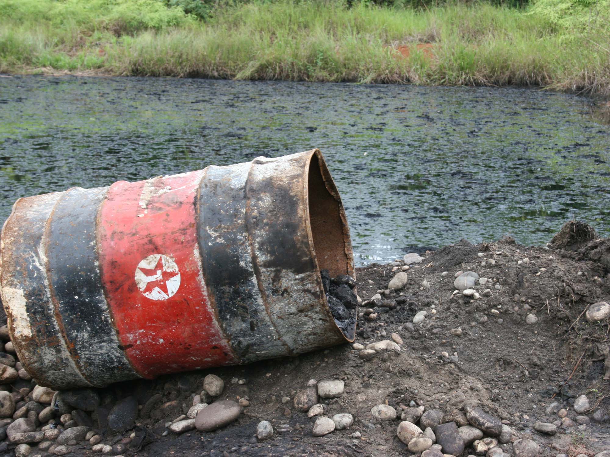 Rusty texaco oil drum next to a polluted river